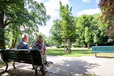 Ein älterer Mann sitzt mit seiner Begleitung auf einer Bank in einem Park